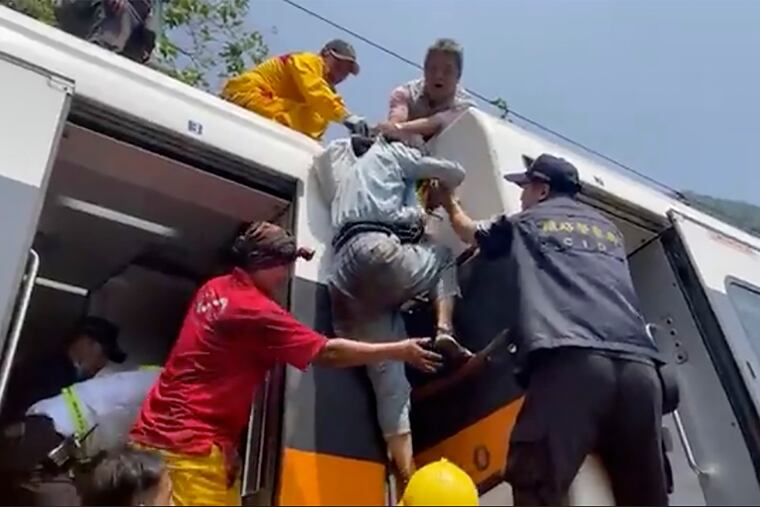 In this image made from a video released by hsnews.com.tw, a passenger (center) is helped to climb out of a derailed train in Hualien County in eastern Taiwan on Friday.