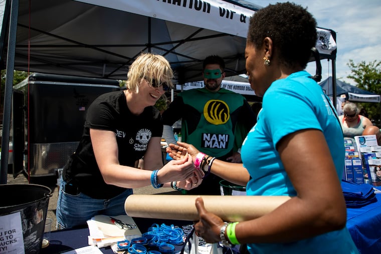Christine Rieck, 47, of Broomall, helps Ariya McGrew, of Brooklyn, N.Y., with her wrist band at the tailgate last month.