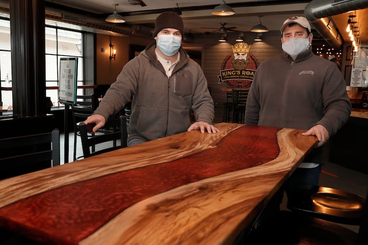 Woodworker Jeff Braddock (left) and Kings Road Brewing Company owner Bob Hochgertel admire a table made from a buttonwood tree that stood in downtown Haddonfield, NJ for 250 years. Pieces of the tree have been salvaged and made available for use by local artisans as part of a grassroots movement to upcycle wood from fallen or removed trees. Braddock, of Moorestown, designed and handcrafted the table for the brewing company.