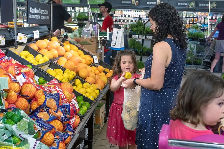 Mother and daughter, 5, pick lemons from a bin at their local Giant supermarket as the 3-year-old waits in the shopping cart.