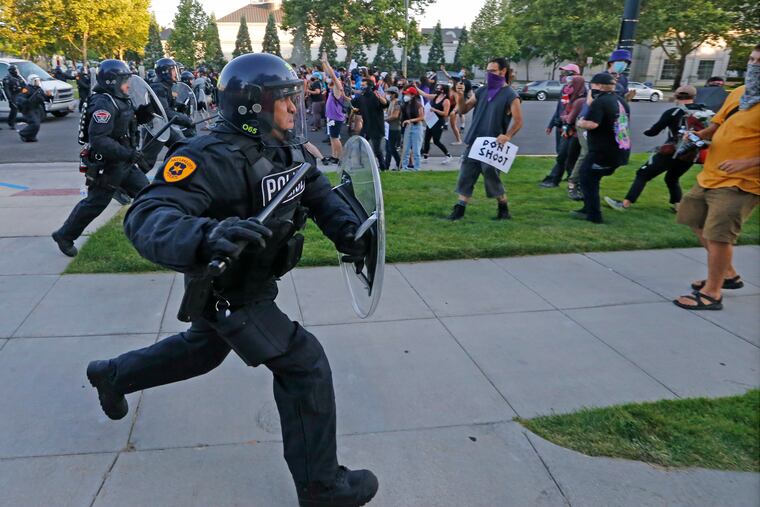 Police officers running toward protesters near the district attorney's office Thursday in Salt Lake City.