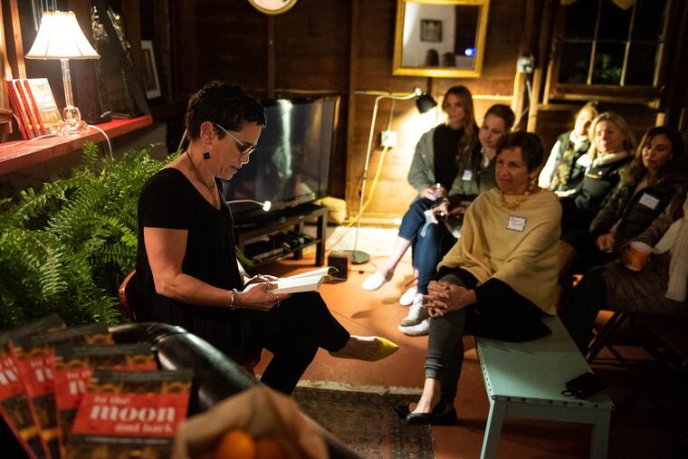 Lisa Kohn, a leadership consultant and coach from Wayne, reads an excerpt from her book, to the moon and back, at a gathering at home of neighbor Elaine Marnell (right, front).