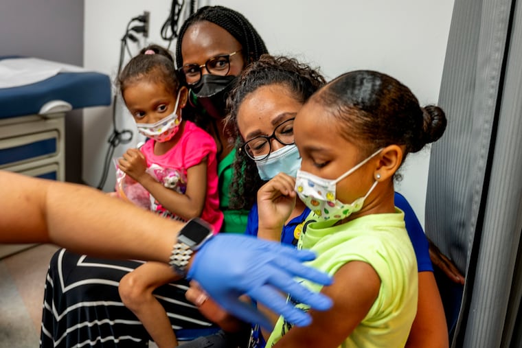 Isabella Aguilar, 8, (front) is held by Celines Mendez as she receives her COVID-19 vaccination at the María de los Santos Health Center on Thursday. Isabella's sister, Iveanna Aguilar, 5, is held by U.S. Department of Health and Human Services Region 3 Director Ala Stanford (rear), who was visiting the Fairhill health center on her tour of sites where the vaccines are available for children under 5.