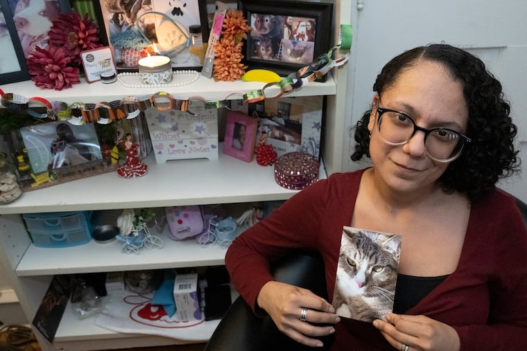 Genesis Pimentel-Howard holds a photo of her late cat, Mobi, beside a lovingly crafted "ofrenda" in her Philadelphia home on Monday. The altar glows with candlelight, welcoming the spirits of her beloved departed pets. The ritual is part of a growing tradition tied to Día de los Muertos.