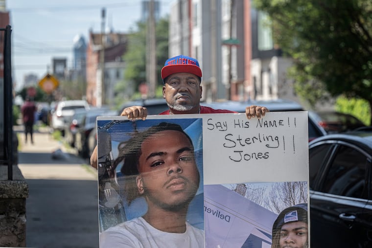 Sterling Lamont Jones Sr. holds a memorial board featuring photographs of his son, on June 5 near the 1300 block of North Broad Street in Philadelphia.