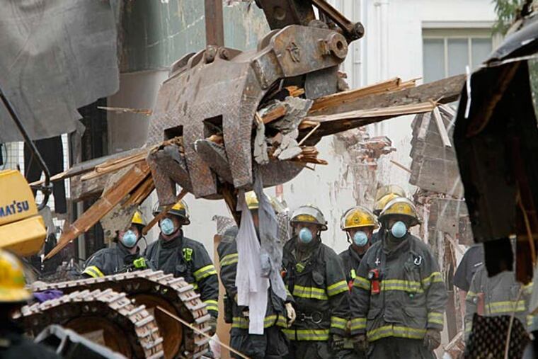 Firefighters watch as a backhoe removes debris from within the collapsed building.