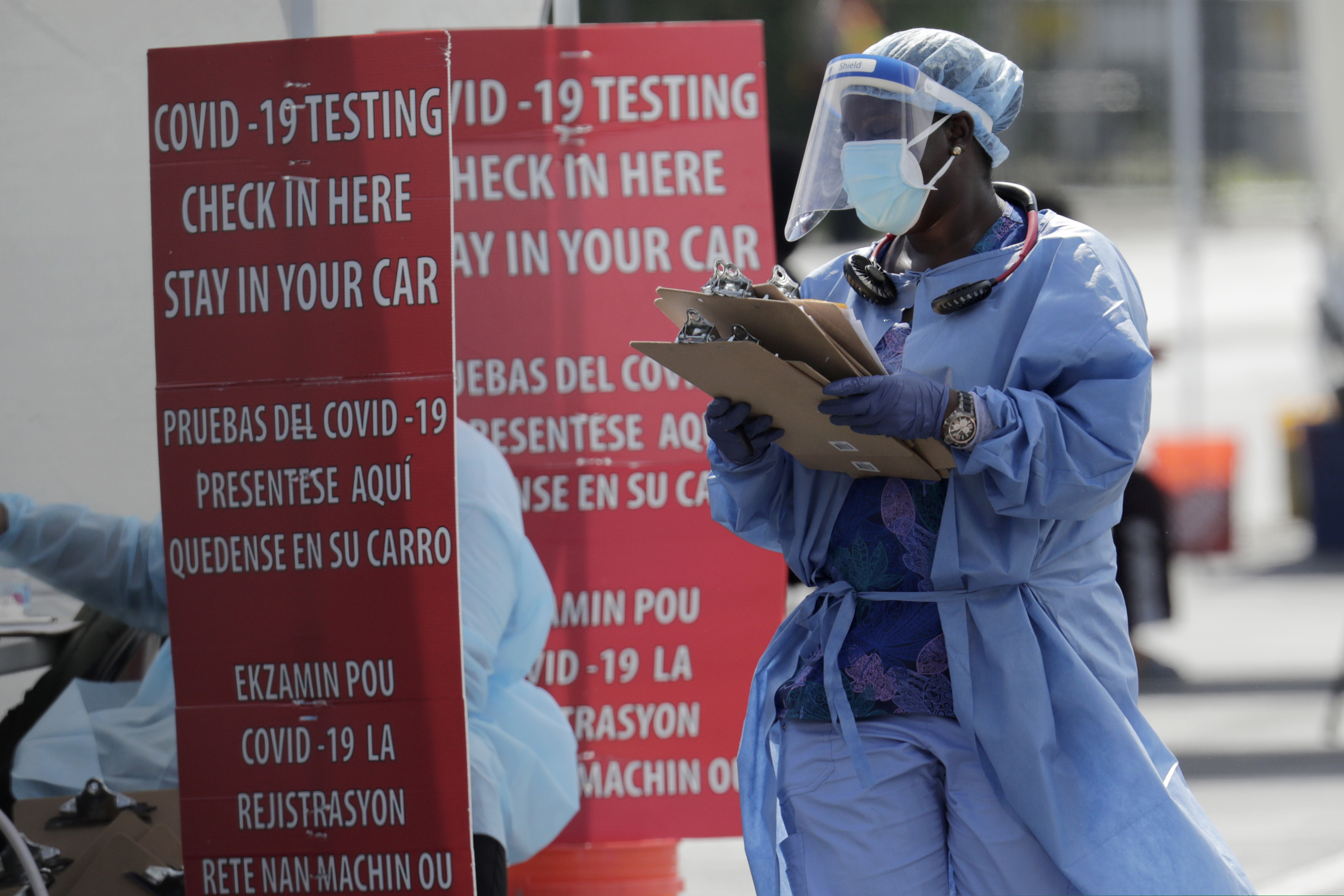 A health care worker carries a stack of clipboards at a COVID-19 testing site sponsored by Community Heath of South Florida at the Martin Luther King, Jr. Clinica Campesina Health Center, during the coronavirus pandemic, Monday, July 6, 2020, in Homestead, Fla. (AP Photo/Lynne Sladky)