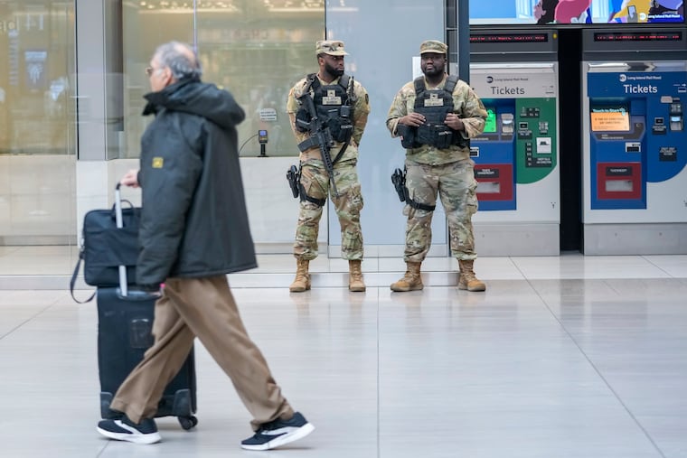 A commuter walks past a couple of New York National Guards soldiers stand guard a the Moynihan Train Hall at Penn Station, Thursday, March 7, 2024, in New York. New York Gov. Kathy Hochul announced plans Wednesday to send the National Guard to the New York City subway system to help police conduct random searches of riders' bags for weapons following a series of high-profile crimes on city trains.