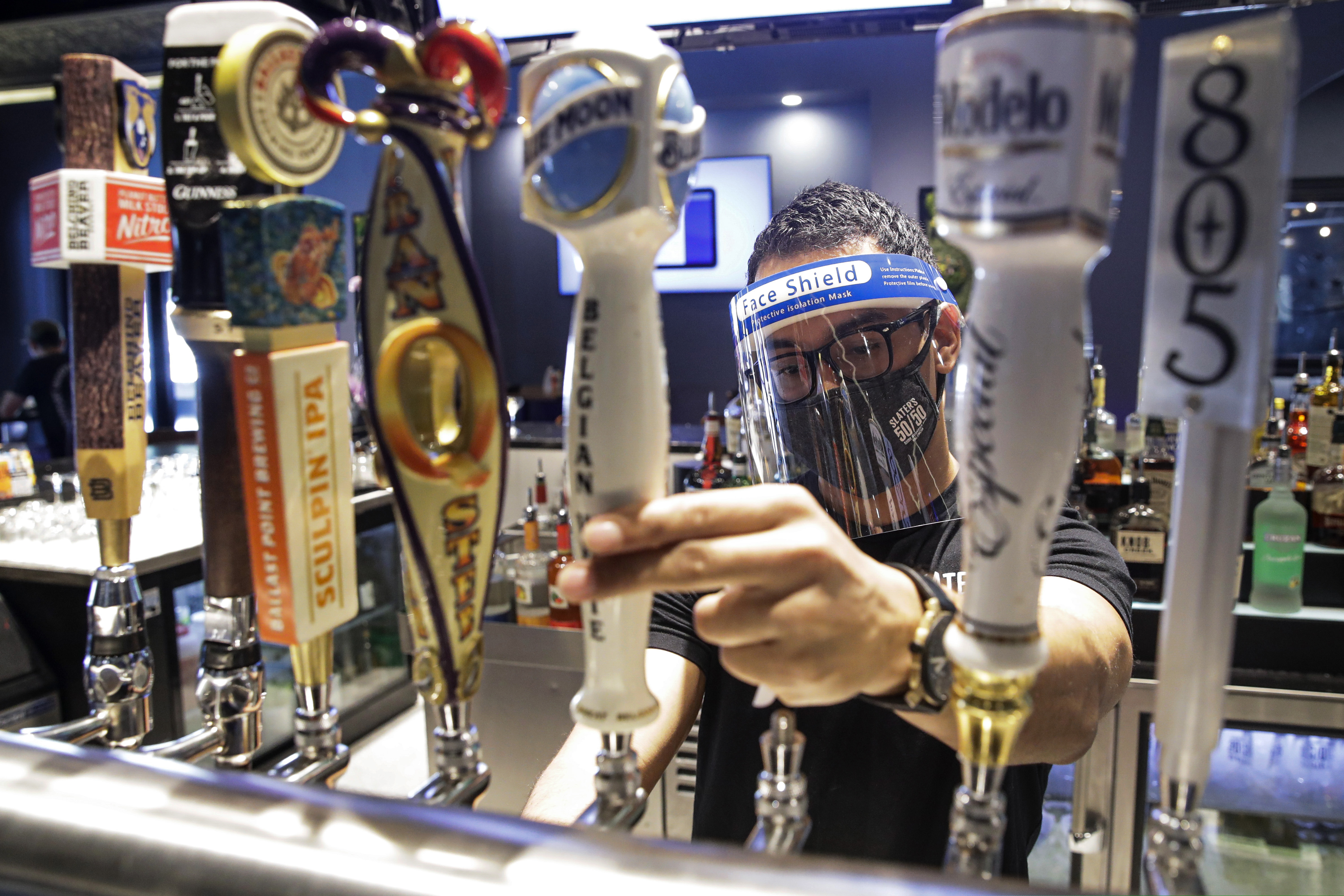 A bartender pours a beer while wearing a mask and face shield amid the coronavirus pandemic at Slater's 50/50 Wednesday, July 1, 2020, in Santa Clarita, Calif. According to a new poll, Americans overwhelmingly are in favor of requiring people to wear masks around other people outside their homes, reflecting fresh alarm over spiking infection rates. The poll also shows increasing disapproval of the federal government's response to the pandemic.