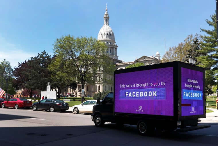 A video sign about Facebook is shown on a truck at the State Capitol during a rally in Lansing, Mich., Wednesday, May 20, 2020. Barbers and hair stylists are protesting the state's stay-at-home orders, a defiant demonstration that reflects how salons have become a symbol for small businesses that are eager to reopen two months after the COVID-19 pandemic began. (AP Photo/Paul Sancya)