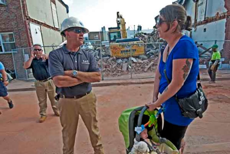 In Philadelphia, Erika Risko-Brannan and son Alister Brannon, 9 weeks, return to their home at 429 Daly Street, directly across from the wreckage of the gas explosion on July 30, 2013. Here, she talks to an L & I employee at the scene. ( APRIL SAUL / Staff )