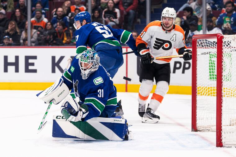 Vancouver goaltender Arturs Silovs redirects the puck into the corner while the Canucks' Tyler Myers and the Flyers' Scott Laughton watch during the first period Saturday.
