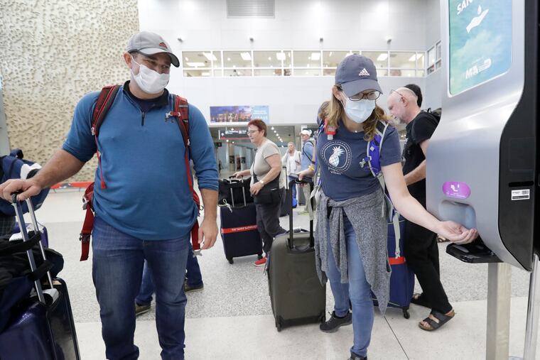 Linda Scruggs, right, applies hand sanitizer as Mike Rustici, left, watches after they arrived on a flight from Lima, Peru, Saturday, at Miami International Airport in Miami.