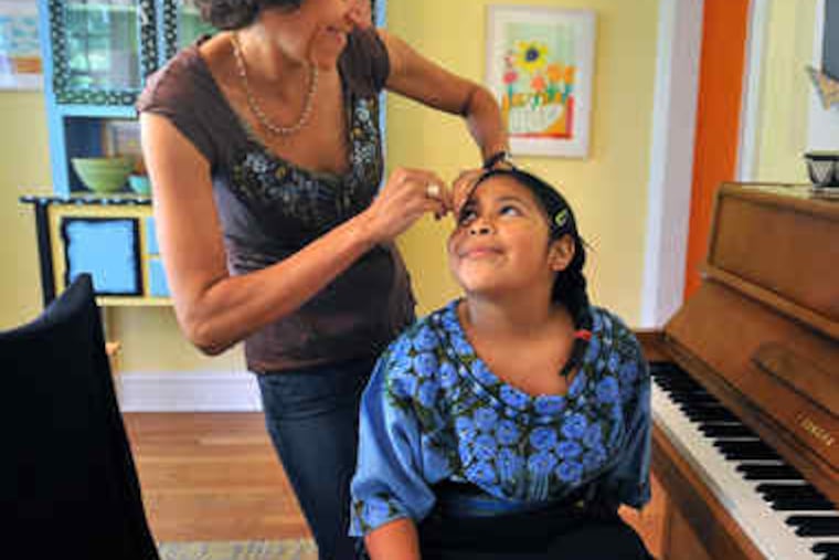 Back home in Mount Airy after their trip, Chloe Cohen wears clothing brought from Guatemala as her adoptive mother fixes her hair.