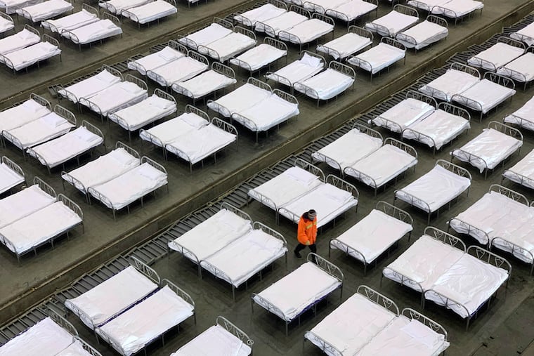 Workers arrange beds in a convention center that has been converted into a temporary hospital in Wuhan in central China's Hubei Province, Tuesday, Feb. 4, 2020. China said Tuesday the number of infections from a new virus surpassed 20,000 as medical workers and patients arrived at a new hospital and President Xi Jinping said "we have launched a people's war of prevention of the epidemic."