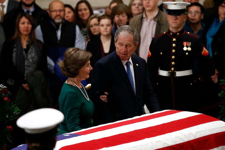 Former President George W. Bush glances toward former first lady Laura Bush as they pause in front of the flag-draped casket of former President George H.W. Bush as he lies in state in the Capitol Rotunda in Washington, Tuesday, Dec. 4, 2018.