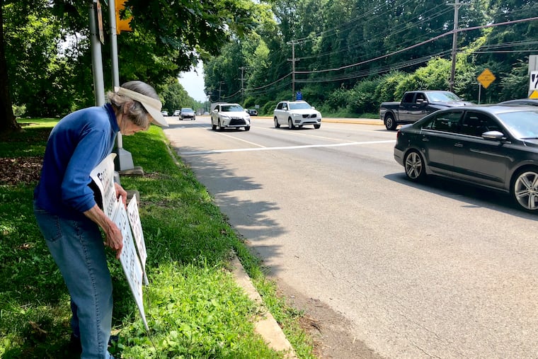 Joan Nicholson, 85, stakes one of her handmade political signs into the grass along Route 1, or Baltimore Pike, in Kennett Square. Nicholson, a longtime peace activist, has been silently standing with these signs every day for 11 consecutive summers.