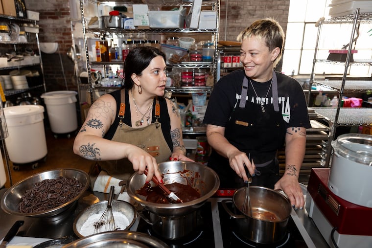 Christina Lower (left) mixes batter while Em Wilson makes caramel at Globe Dye Works on June 12 in Philadelphia. Lower, the owner of Kensington-based Bake Bake Philly, and Wilson, owner of West Philly-based Em Wilson Pastry, share a kitchen near Frankford.