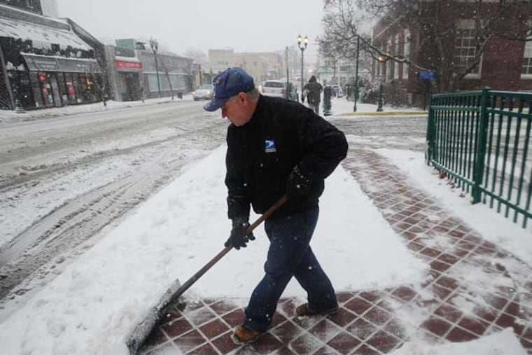 USPS worker Jiuseppe Gramuglia cleans snow, not far from the post office on Main Street in Fort Lee, N.J. as a winter storm hits the region on Friday, Feb. 8, 2013. (AP Photo/The Record of Bergen County, Marko Georgiev)