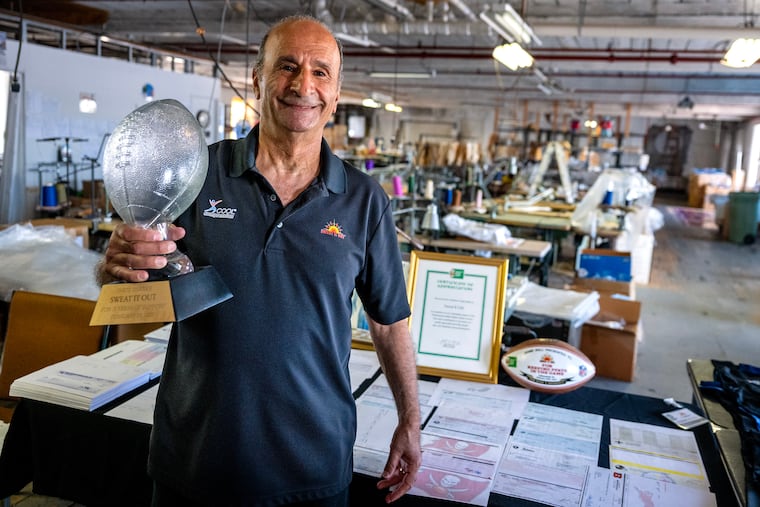 Efraim Nathan at his Sweat It Out shop in Norristown Wednesday, Sept. 11, 2024, with an award from the Professional Football Athletic Trainers Society. He is proud of his many honors from the PFATS, a group of certified athletic trainers in the National Football League that have collaborated in the area of player health and safety for over 60 years. A federal court said Nike illegally copied his compression technology and produced cheap knockoff designs. The documents on the table are some of the many used to support his lawsuit.