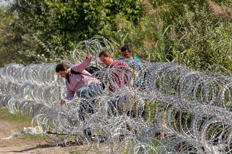Migrants jump over razor wire strung along the border, where Hungarian soldiers have already laid low-level fortifications.