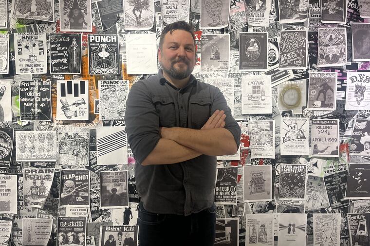 Justin Gray, co-curator of "Shortest, Fastest, Loudest," stands in front of the flier wall at Stockton University.