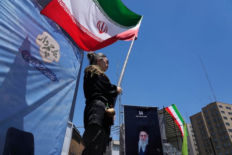 A woman waves an Iranian flag during a pro-government campaign as a portrait of the slain Supreme Leader Ayatollah Ali Khamenei, who was killed in U.S. and Israeli strikes on Feb. 28, is displayed at right, in downtown Tehran, Iran, Monday, June 15, 2026.