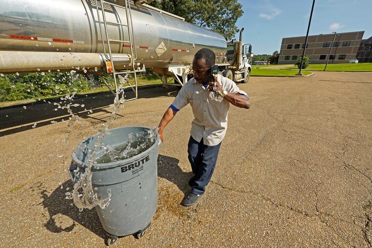 Santonia Matthews, a custodian at Forest Hill High School in Jackson, Miss., hauls away a trash can filled with water from a tanker in the school's parking lot, Wednesday.