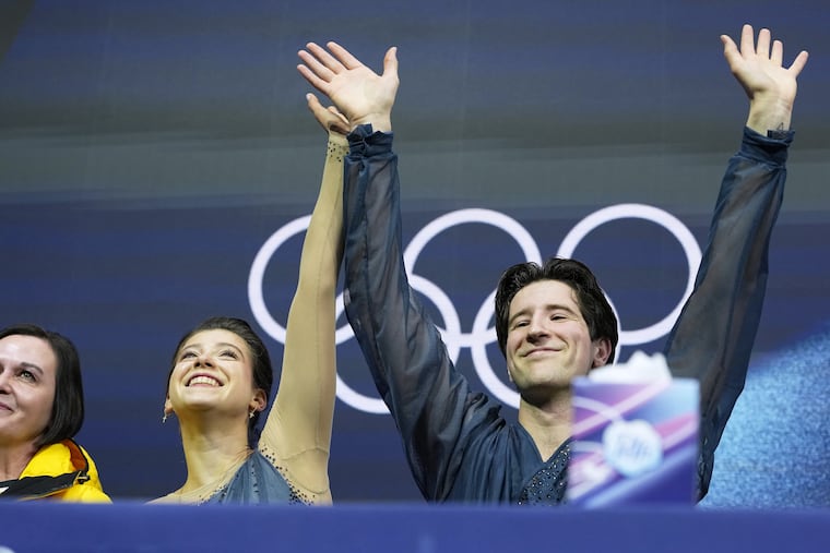 Anastasiia Golubeva and Hektor Giotopoulos Moore of Australia wait for scores after competing in the pairs figure skating short program at the 2026 Winter Olympics, in Milan, Italy, on Sunday. A box of Puffs tissues is prominently placed.