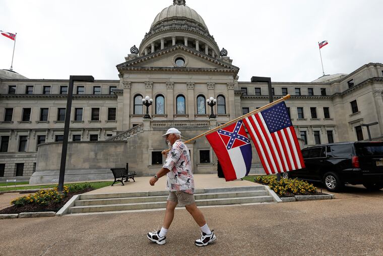 Don Hartness of Ellisville, walks around the Capitol carrying the current Mississippi state flag and the American flag, Saturday, June 27, 2020, in Jackson, Miss. The current state flag has in the canton portion of the banner the design of the Civil War-era Confederate battle flag, that has been the center of a long-simmering debate about its removal or replacement.