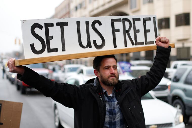 Steve Polet holds a sign during a protest at the State Capitol in Lansing, Mich., on Wednesday over economic restrictions to curb the spread of the coronavirus. In Pennsylvania, Republican lawmakers pushed Gov. Tom Wolf to lift restrictions.