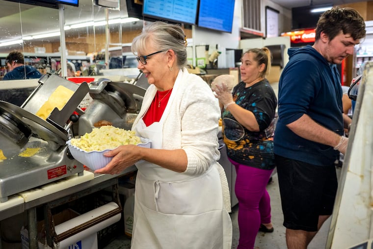 John's Friendly Market co-owner Josie Doto (left) carries freshly made potato salad to the deli at the store in Haddon Heights. Behind her are deli workers Clare Hendricks and Chris Hangan.