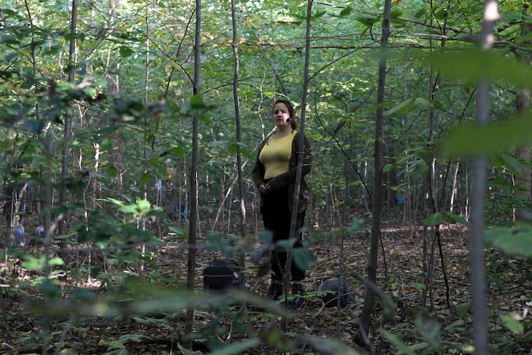 A member of The Crossing choir stands among the trees of the Bowman's Hill Wildflower Preserve. The choir performed for audience members who listened to vertical speakers set up throughout the forest in New Hope, PA, October 3, 2020.
