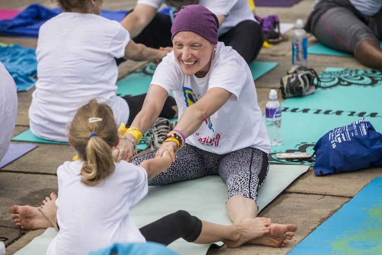 Three days after her final chemotherapy treatment, Kim Daniels, 41, of Chestnut Hill, stretches with daughter Jasmine, 7, at the Philadelphia Art Museum as part of the Reach & Raise fund-raiser for Living Beyond Breast Cancer.
