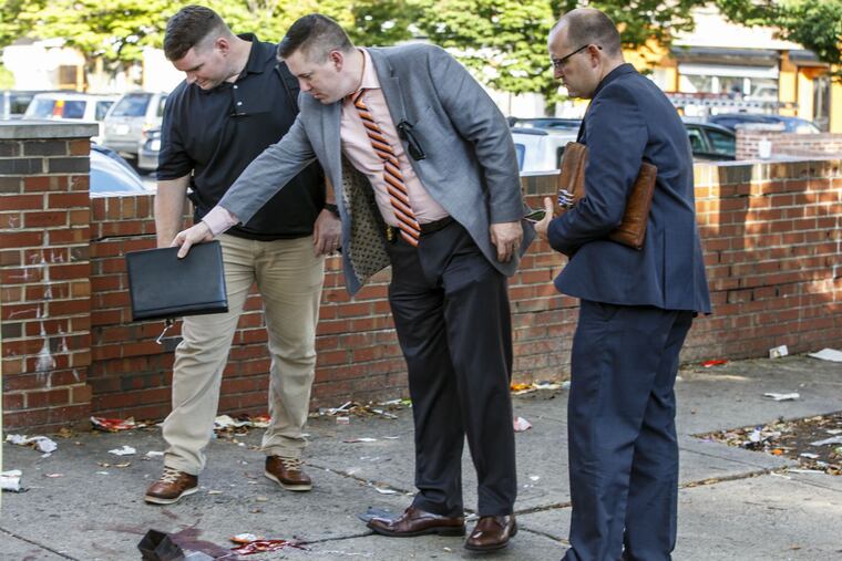 Philadelphia Police Dectectives stand over a pool of blood on the sidewalk on Germantown Avenue, near Wister Street, where five people were shot on Wednesday, October 3, 2018, when an assailant jumped out of car, opened fire and left the scene.