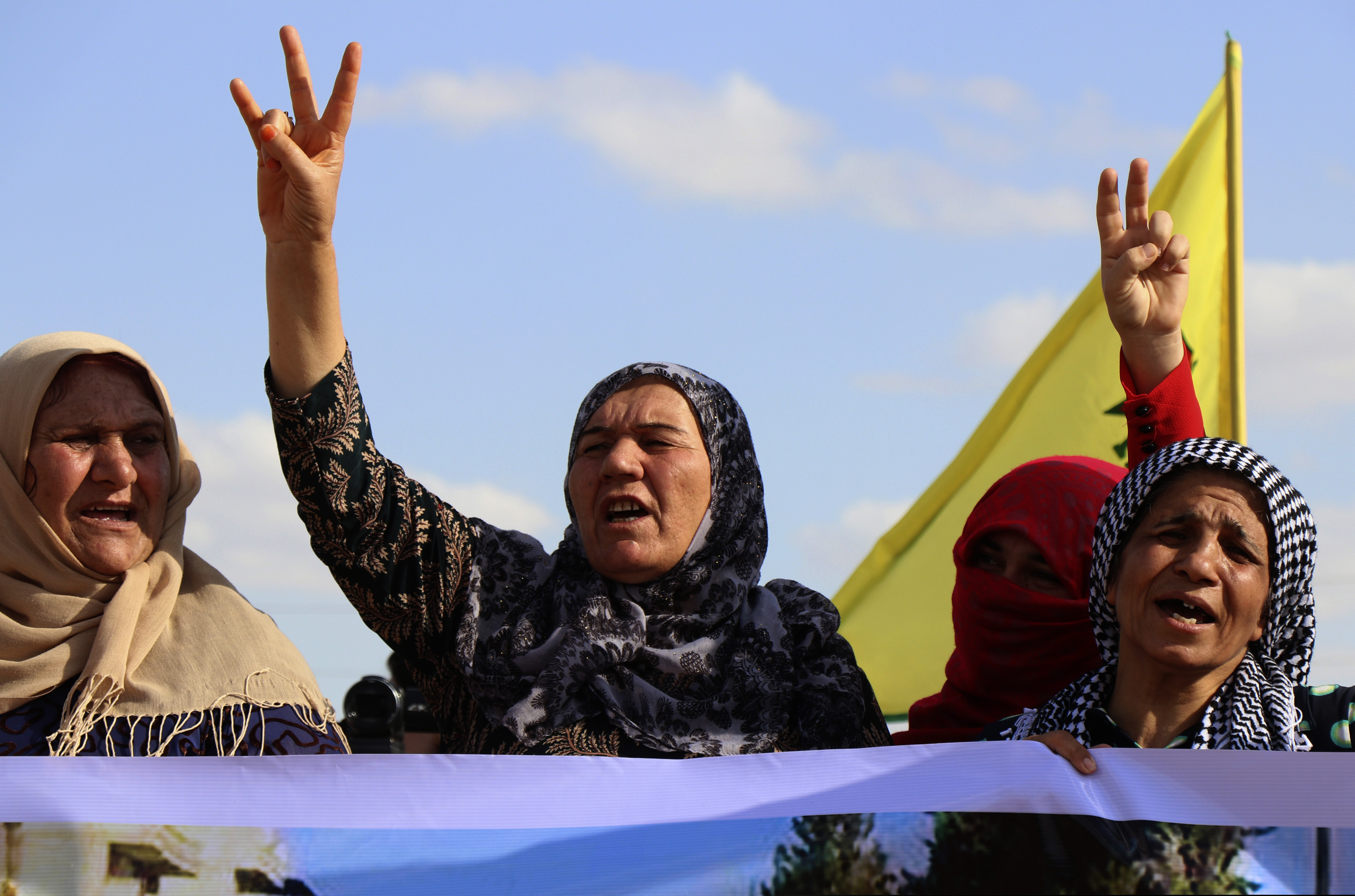 Kurdish women flash victory signs and shout slogans as they protest against possible Turkish military operation on their areas, at the Syrian-Turkish border, in Ras al-Ayn, Syria, Monday, Oct. 7, 2019. Syria's Kurds accused the U.S. of turning its back on its allies and risking gains made in the fight against the Islamic State group as American troops began pulling back on Monday from positions in northeastern Syria ahead of an expected Turkish assault.