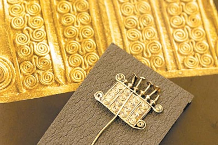 A brooch from the University of Pennsylvania collection is shown against a picture of one known to be from Troy. (CHARLES FOX / Staff Photographer)