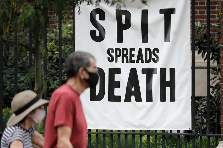 A couple walks by a sign for "Spit Spreads Death: The Influenza Pandemic of 1918-19 in Philadelphia" an exhibit at the Mütter Museum of the College of Physicians of Philadelphia. Museums are shuttered under new COVID restrictions.