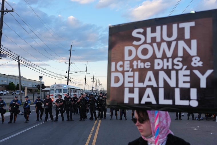 A protester holds a sign as law enforcement officers stand outside Delaney Hall detention center on Sunday, May 31, 2026, in Newark, N.J.