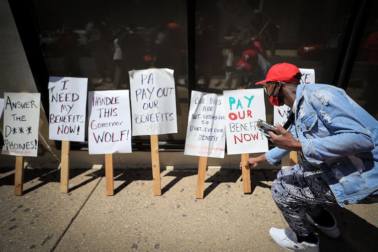 Reggie Moore picks up a sign to join unemployed workers as they protest outside of Gov. Wolf’s regional office in Philadelphia in May.