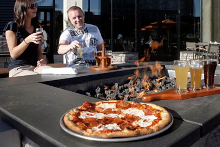 At a fire pit on the rooftop terrace, Natalie Zeppa and Daniel Kalinovski sip from a tasting rack, with a pepperoni pizza near at hand. (AKIRA SUWA / Staff Photographer)