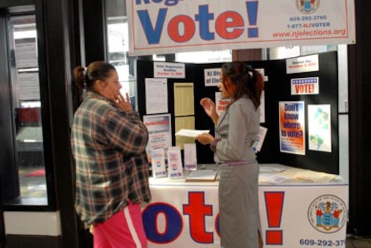 At the Walter Rand Transportation Center in Camden, officials register voters and hand out mail-in voting materials. Here, Madeline Rodriguez, right, gives info to Agripina Vega of Cherry Hill. ( April Saul / Staff Photographer )