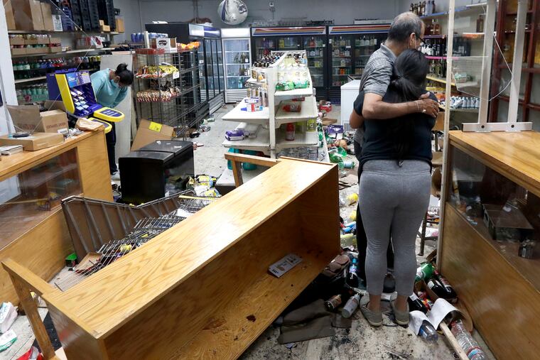 Yogi Dalal hugs his daughter Jigisha as his other daughter Kajal, left, bows her head at the family food and liquor store after the family business was vandalized in Chicago.
