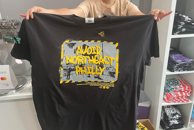 An Art History 101 employee holds up the store's new limited-edition shirt, which reads "Avoid Northeast Philly" and was inspired by the I-95 collapse and indefinite highway closure, on Wednesday June 14 at the shop on Frankford Avenue in Mayfair.