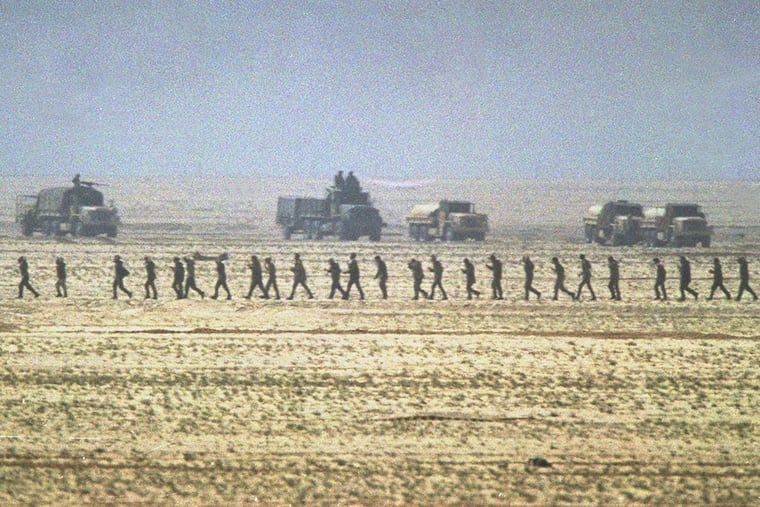 A line of captured Iraqi soldiers are marched through the desert in Kuwait past a group of U.S. Marine Second Division vehicles on Feb. 24, 1991, after the ground offensive got underway during the Persian Gulf War. (AP Photo/Sadayuki Mikami)