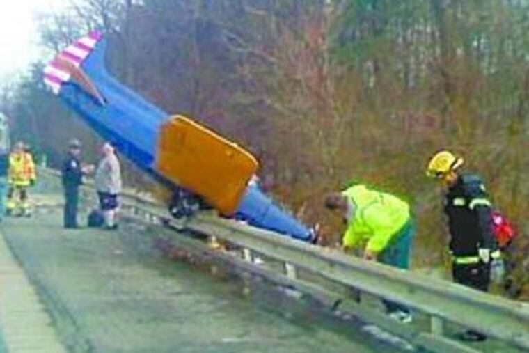 A SMALL PLANE is seen perched over the guardrail on the side of the Pennsylvania Turnpike near Newville, Cumberland County, yesterday. Officials say the pilot, who was taken to a hospital, was experiencing engine trouble.