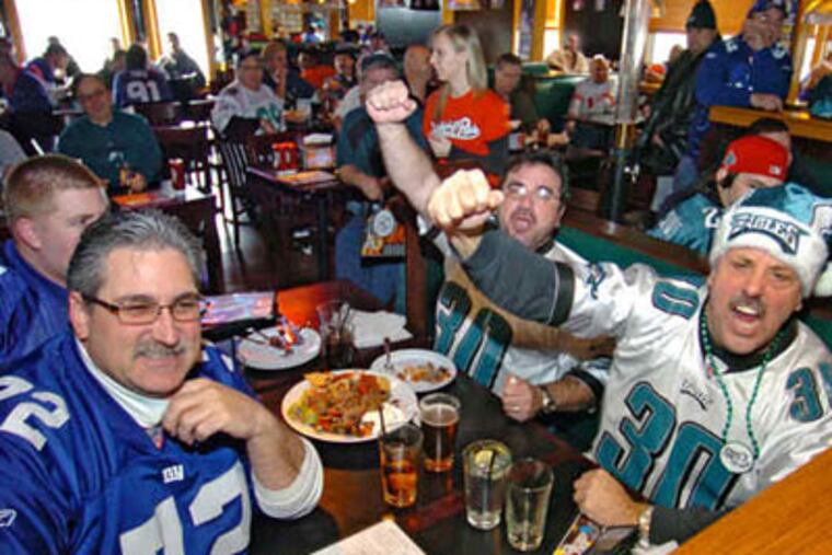 Eagles fans Larry Barnard and Rocco Ricccio (right) lead cheers for their team while across the table former neighbors and Giants fans Joe Zaczek Jr. and his son Joe III wait their turn. (Clem Murray / Staff Photographer)
