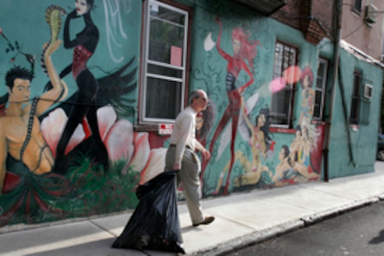Michael Sher drags away a bag of trash that was left in front of the townhouse he manages at 410 S. 15th Street. Partly because of a problem with graffiti, Sher commissioned an artist to paint a mural on the building in 2001, but did not get the proper permits.