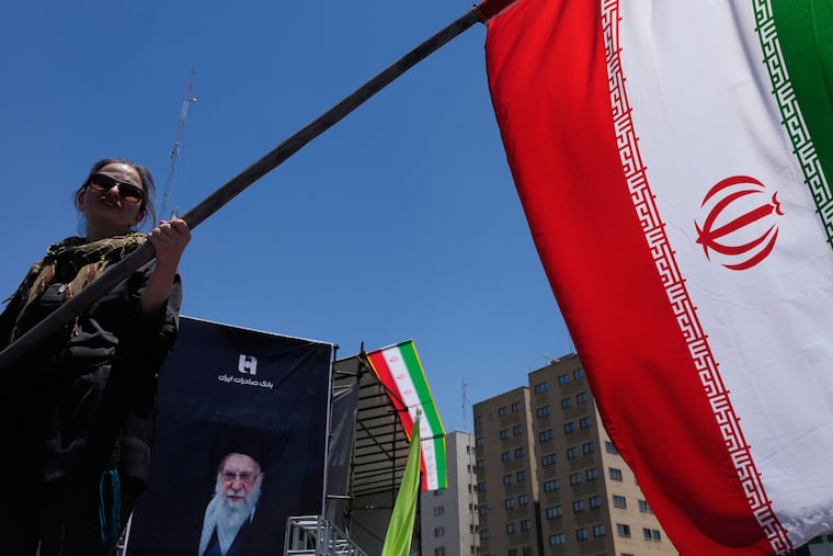 A woman waves an Iranian flag during a pro-government campaign as a portrait of the slain Supreme Leader Ayatollah Ali Khamenei, who was killed in U.S. and Israeli strikes on Feb. 28, is displayed at rear, in downtown Tehran, Iran, Monday, June 15, 2026.