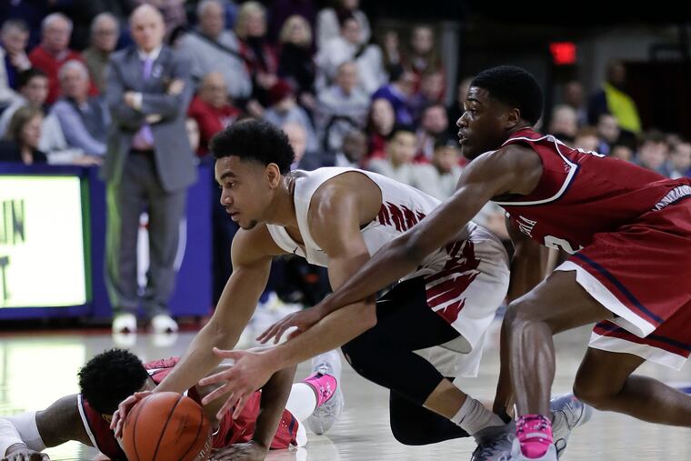 Saint Joseph's Jared Bynum (center) reaches for the loose ball past Penn's Devon Goodman (right) and Antonio Woods during a January game.